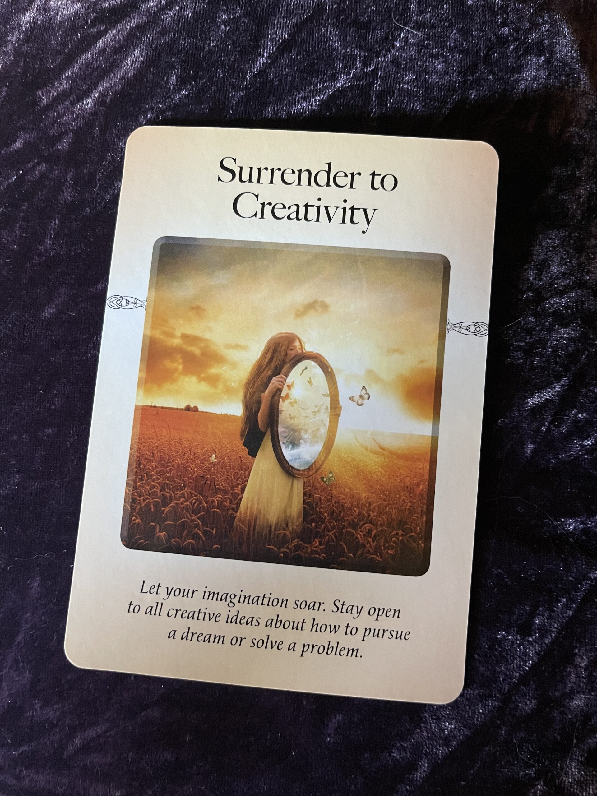 Surrender to Creativity oracle card revealed of a woman in an open field holding a mirror with butterflies for transformation